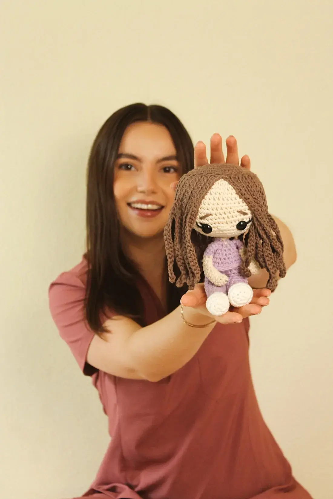 Dani sonriendo mientras extiende hacia la cámara una muñeca tejida a mano