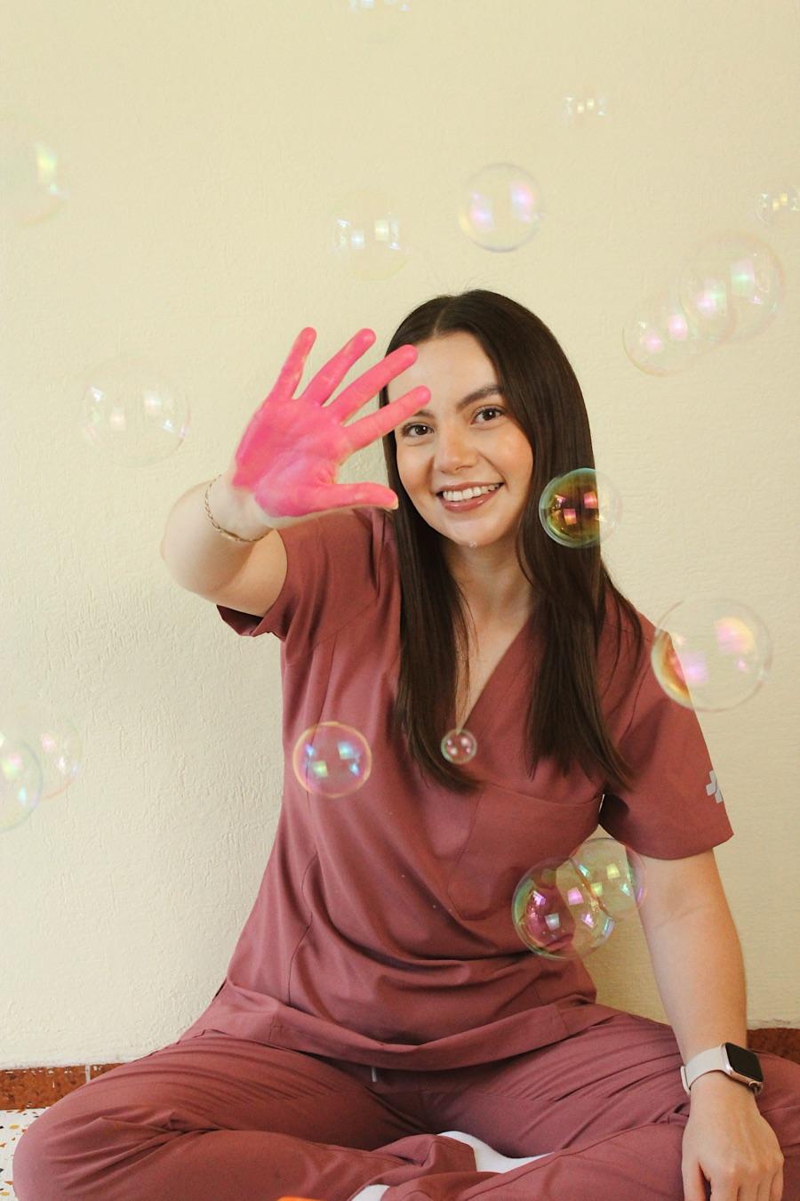 Dani, fisioterapeuta de Brainy Bodies, sonriendo entre burbujas con la mano pintada